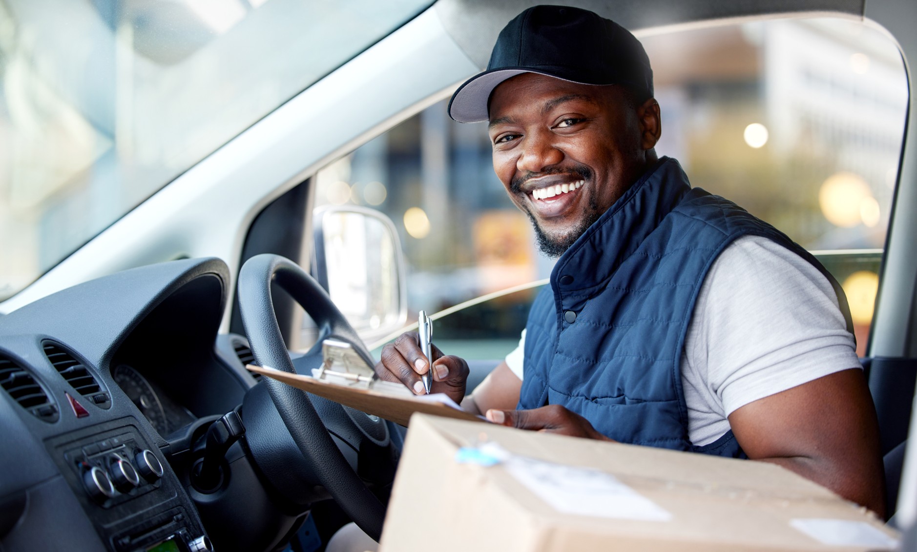 Happy delivery driver in a vehicle with a parcel and clipboard, illustrating the importance of courier and goods in transit insurance in South Africa