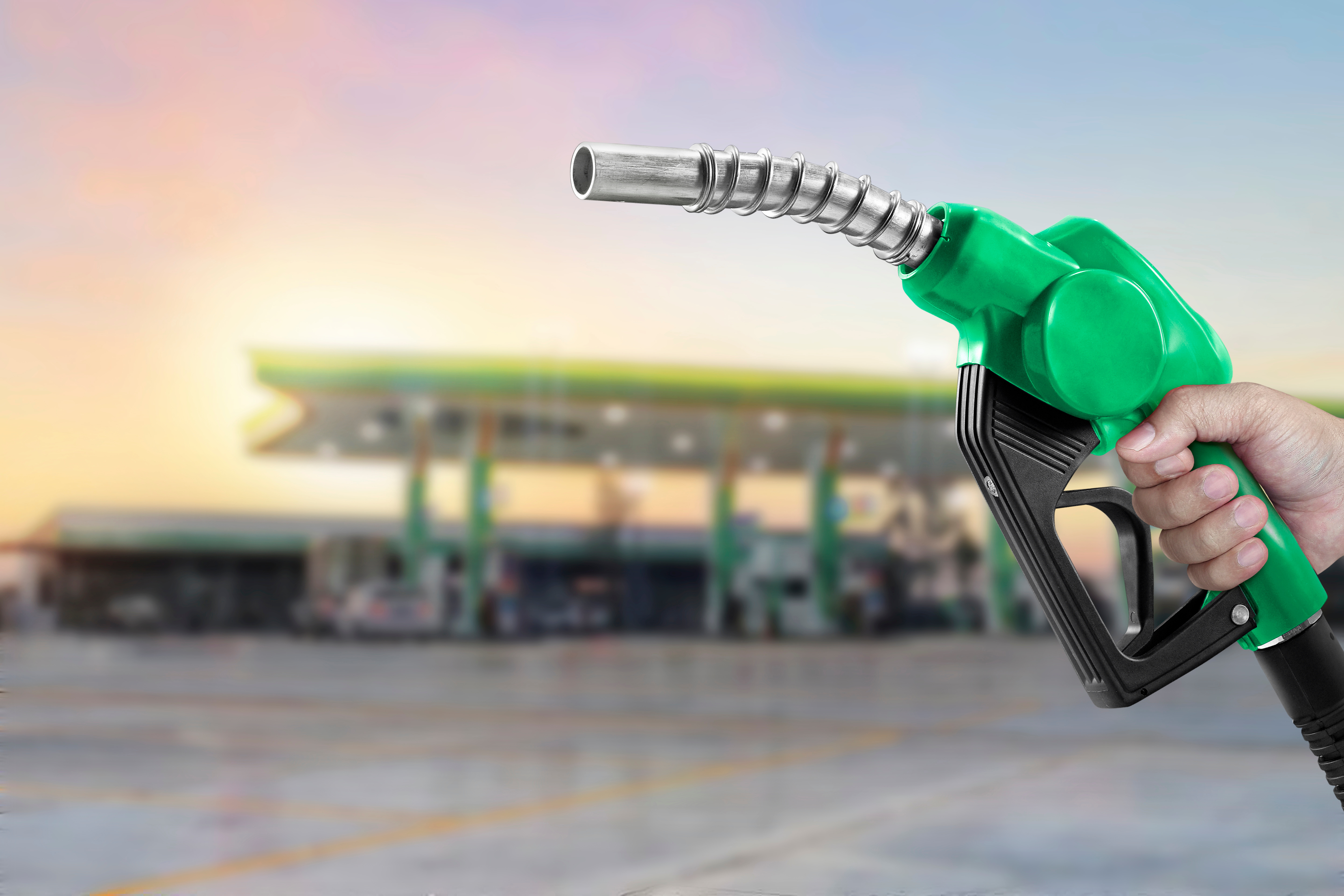 Green fuel nozzle being held at a petrol station during sunset, symbolizing rising South African fuel prices in 2025